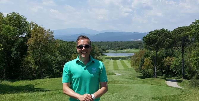 Fraser on a golf course with mountains in the background and a golf club in his hands