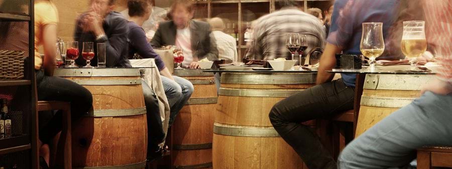 The image shows people in a bar sitting at tables made from barrels.