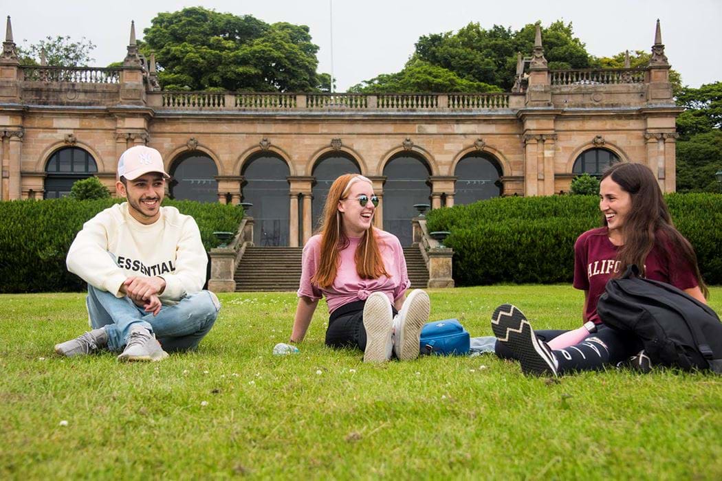 3 students chatting on the grass in the park