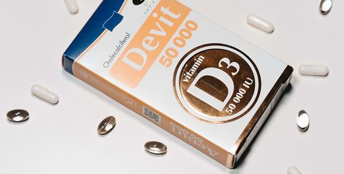 The image shows a box of vitamin D supplements surrounded by pills and capsules.