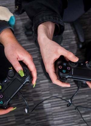 The image shows two hands showing two game pads. One of the hands has painted nails.