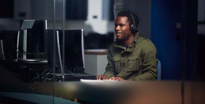 Male student wearing headphones whilst working on a Desktop computer