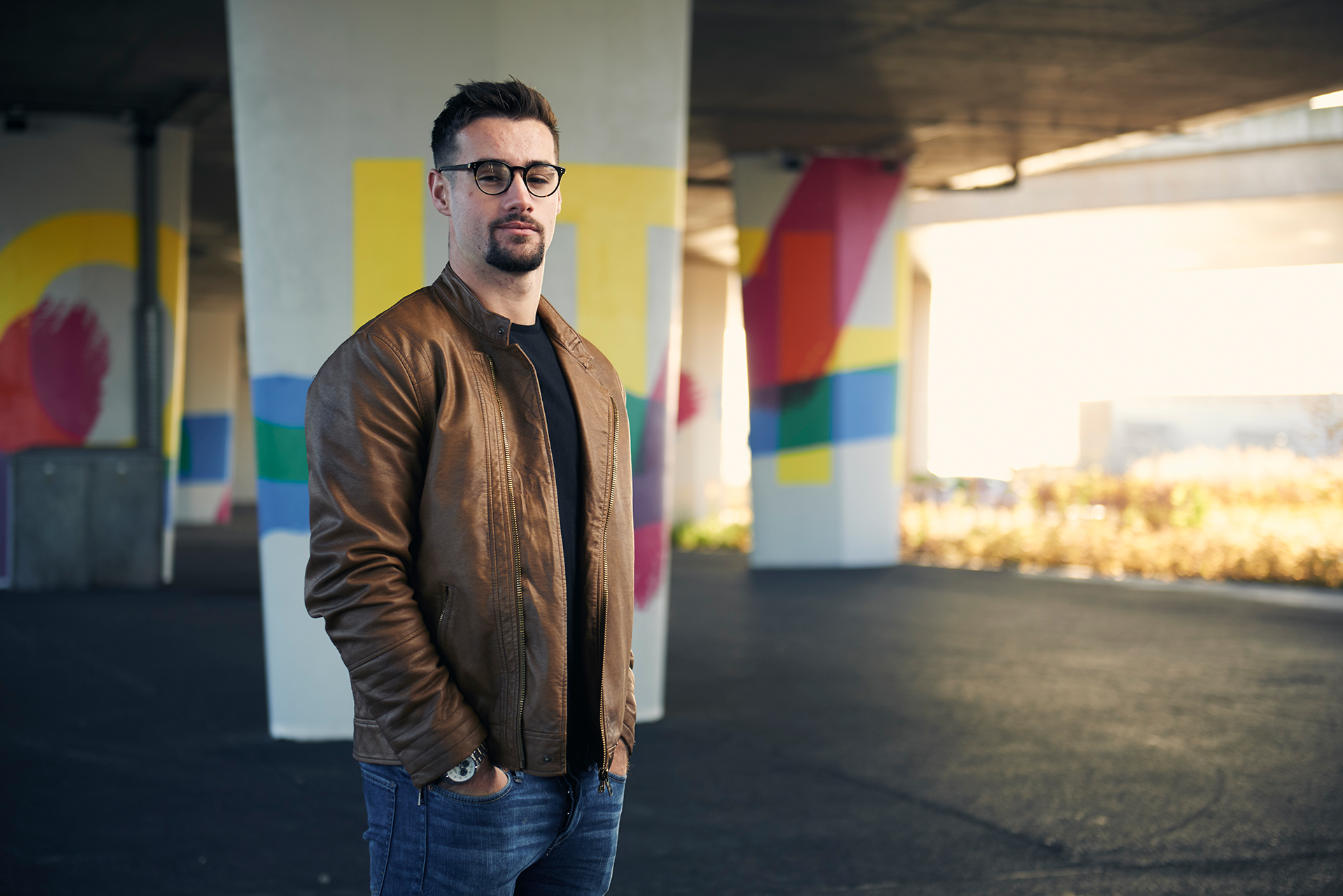 Male with hands in pockets - standing underneath a bridge