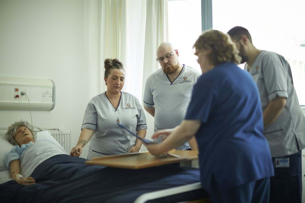 Hospital environment - patient lying in bed and 4 Nursing staff standing around the bed