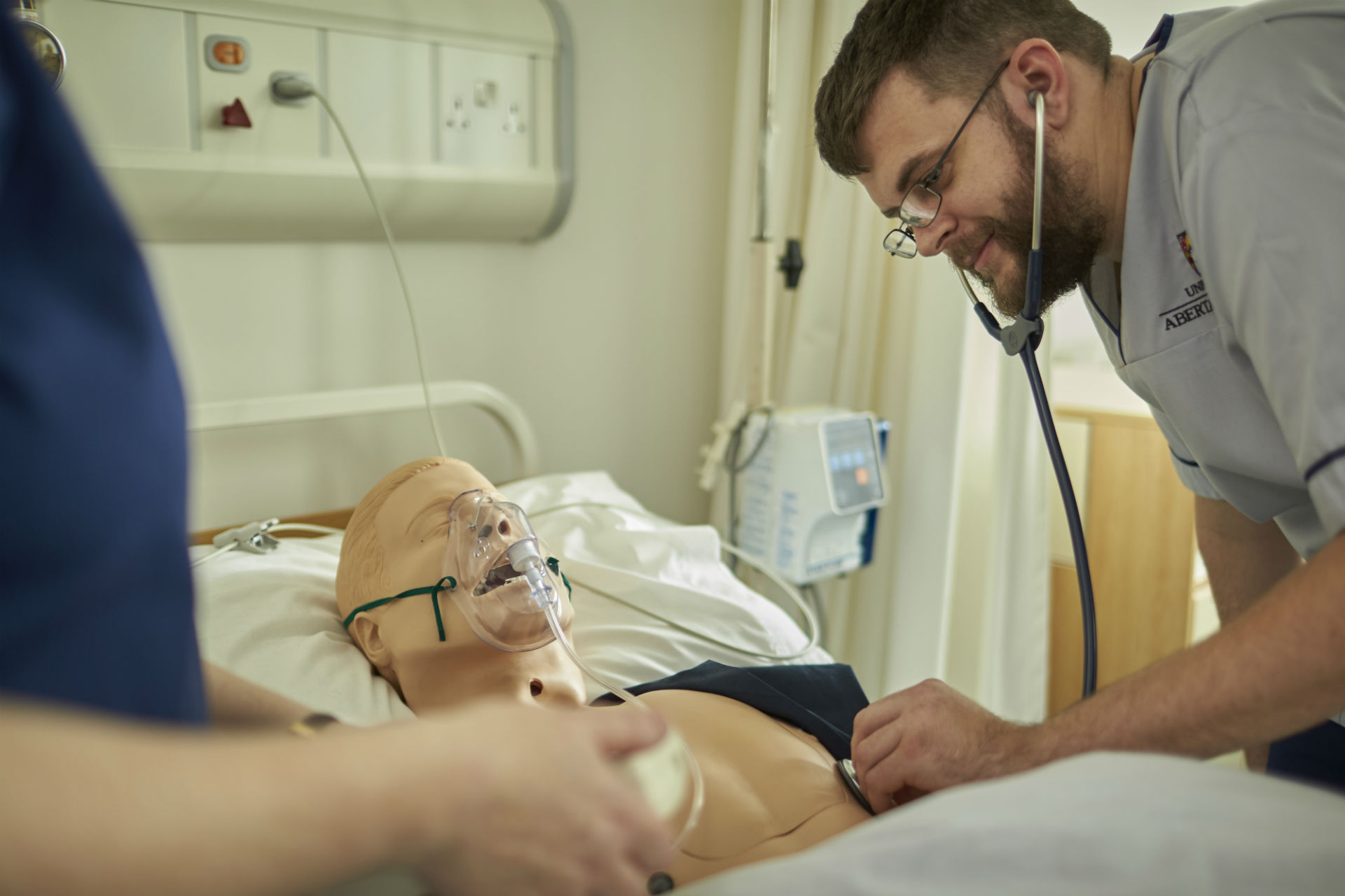 Hospital environment - patient lying in bed and a male Nurse is listening to patients chest via the use of a stethoscope 
