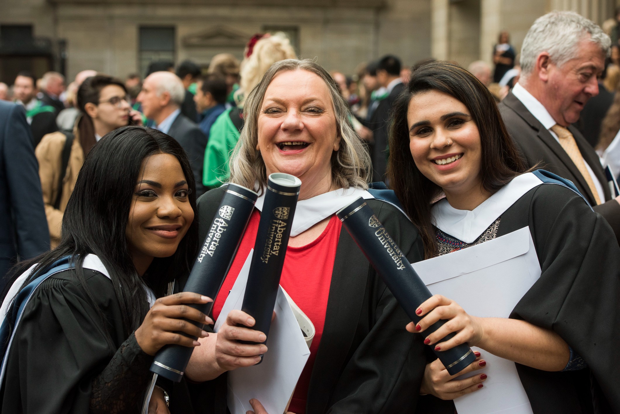 Three female students in graduation gowns holding scrolls