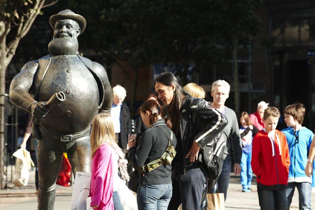 Group of people standing beside the Desperate Dan statue in Dundee City Centre