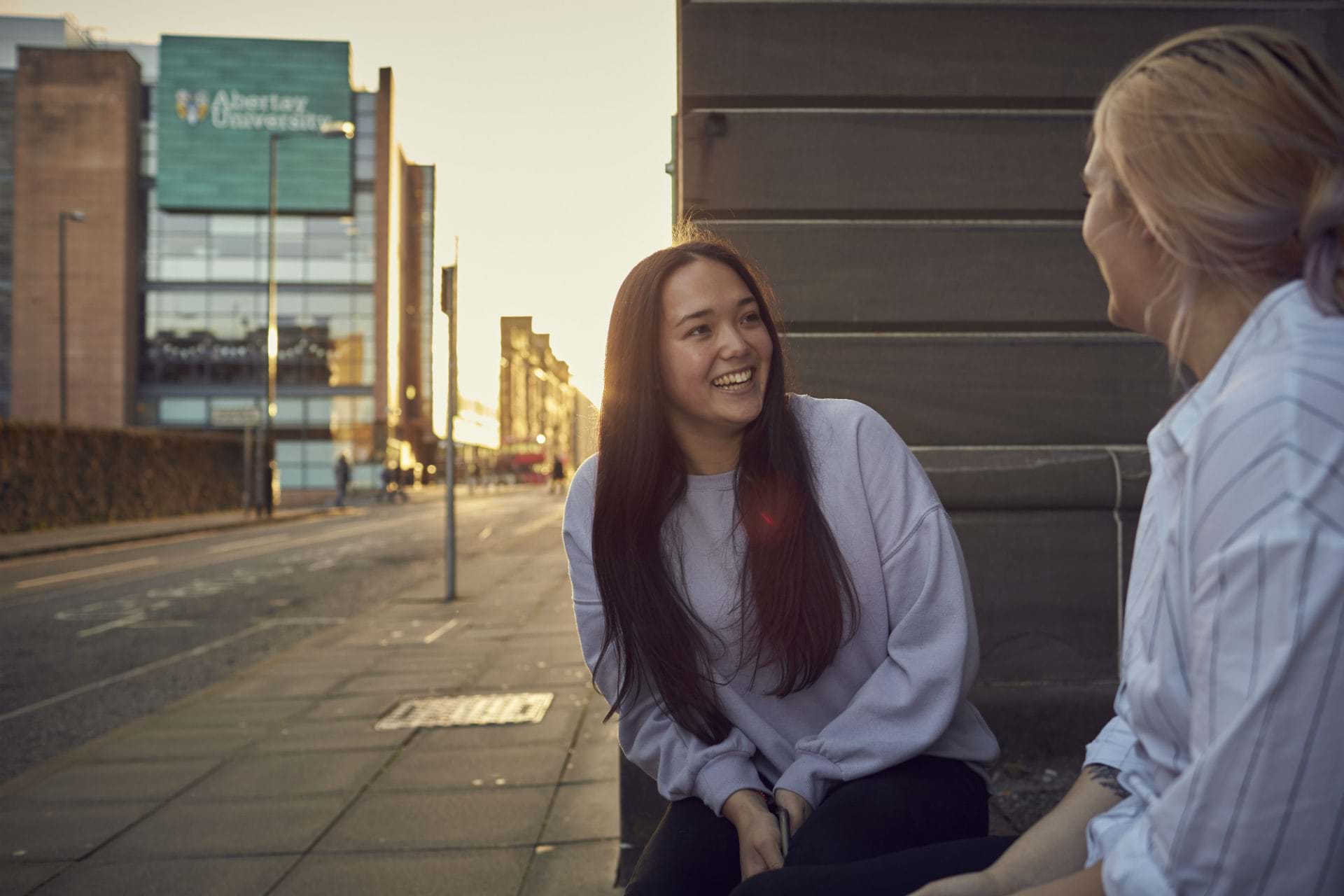 Two students sitting chatting outside Abertay campus 