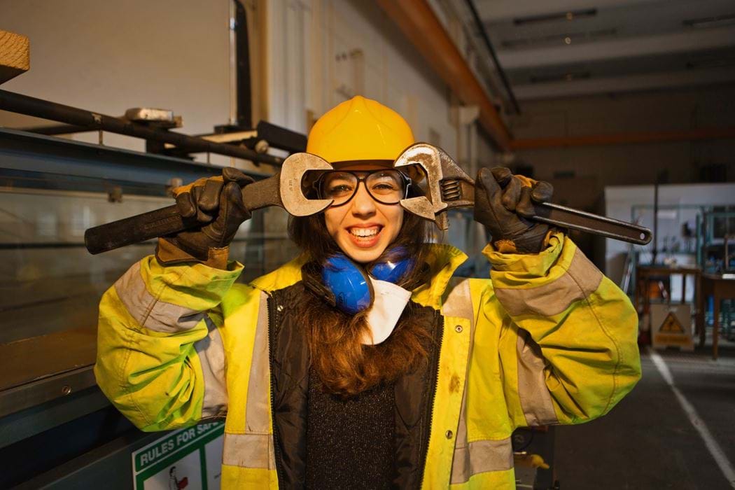 Female engineering student holding wrenches close to face