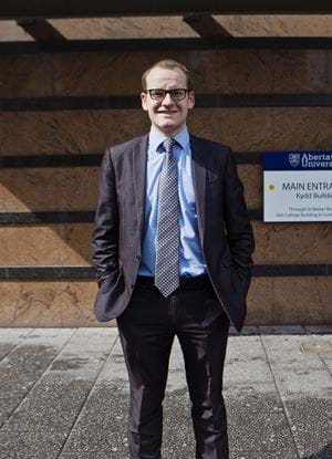 Steven Traynor in a suit standing in front of Abertay University's Kydd building