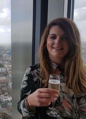 A picture of Linzi Brechin holding a glass of champagne with the view of a large city behind her.
