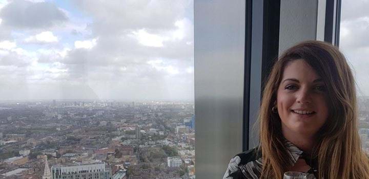 A picture of Linzi Brechin holding a glass of champagne with the view of a large city behind her.