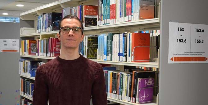 A photo of Nikolay Panayotov in Abertay University library, in front of bookshelves