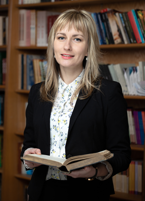 Graduate standing in front of bookshelf holding a book