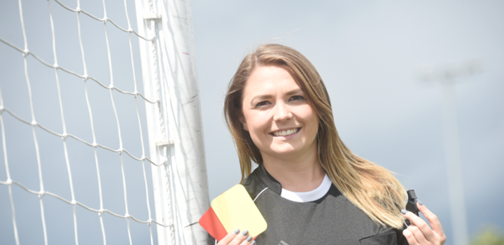 Vikki in FIFA Assistant Referee uniform holding a whistle and cards