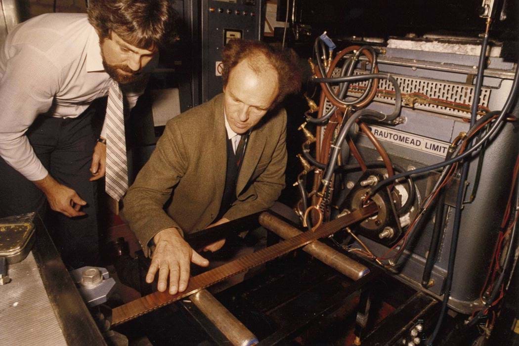 Two men, Dr Bob Johnson, Abertay University, and Sir Michael Nairn, Rautomead Company Ltd., inspecting the 22 carat gold strip emerging from a continuous casting machine at Royal Mint demonstration