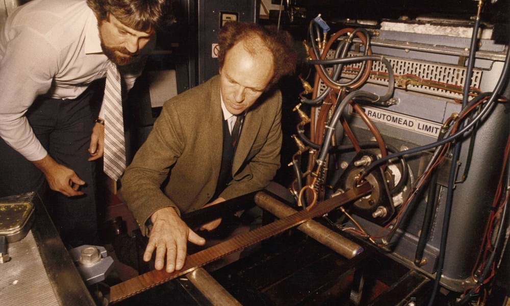 Two men, Dr Bob Johnson, Abertay University, and Sir Michael Nairn, Rautomead Company Ltd., inspecting the 22 carat gold strip emerging from a continuous casting machine at Royal Mint demonstration