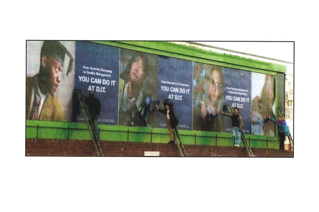 Four Students on ladders in front of their images on a billboard for You Can Do It At D.I.T.