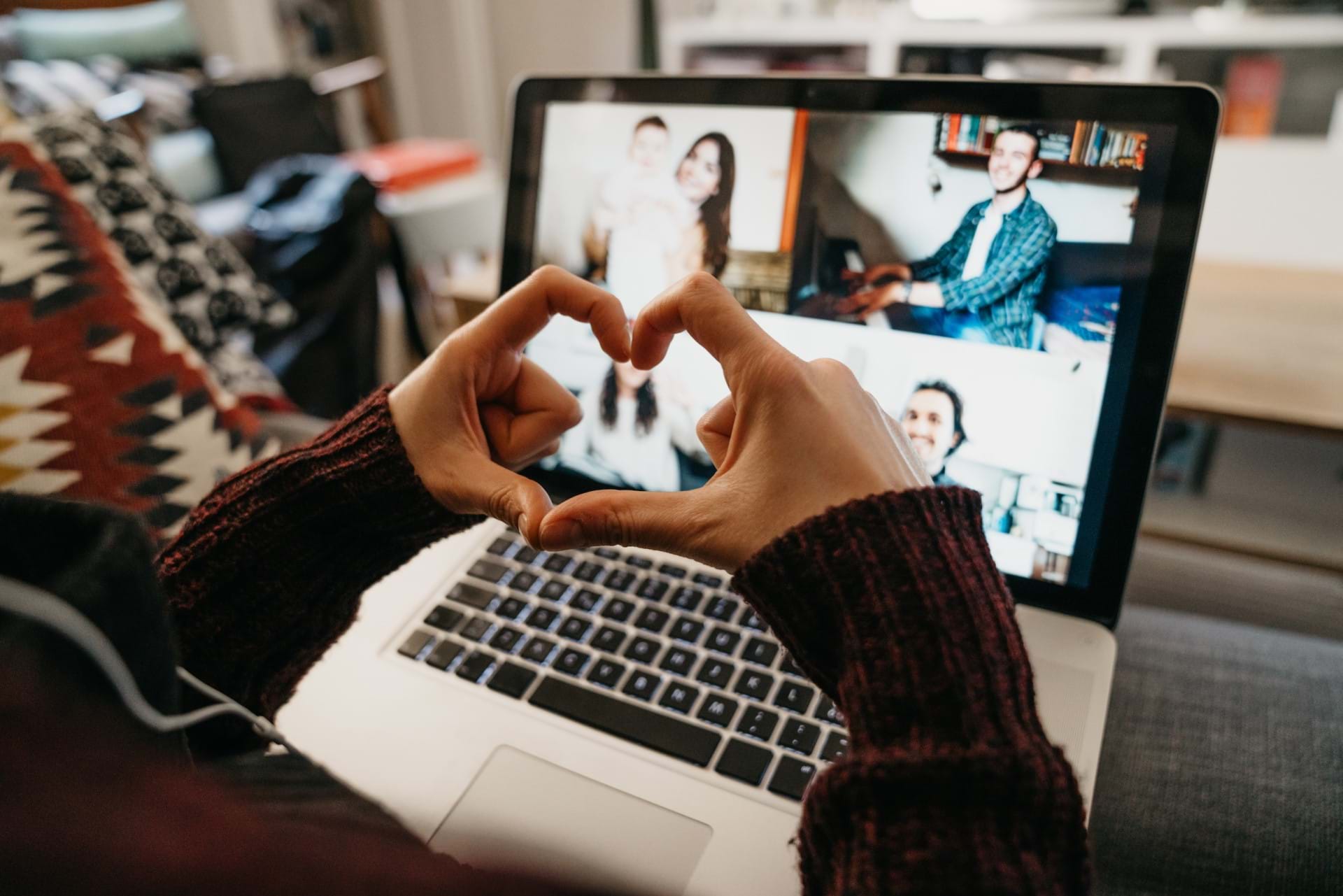 A photo of hands making a heart symbol in front of a laptop