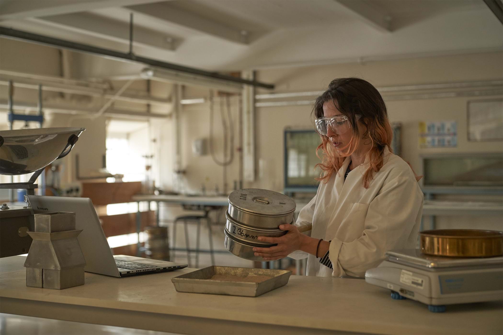 A female student in a food lab wearing protective goggles and a white coat