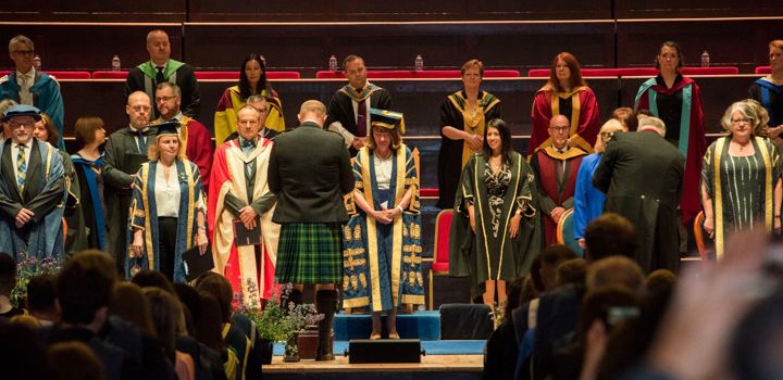 A group of academics standing on the Caird Hall stage for graduation. 