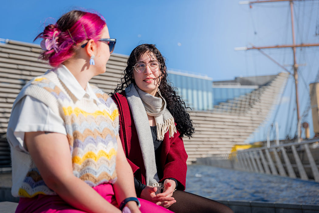 two female students sitting chatting in front of the V&A museum and discovery ship