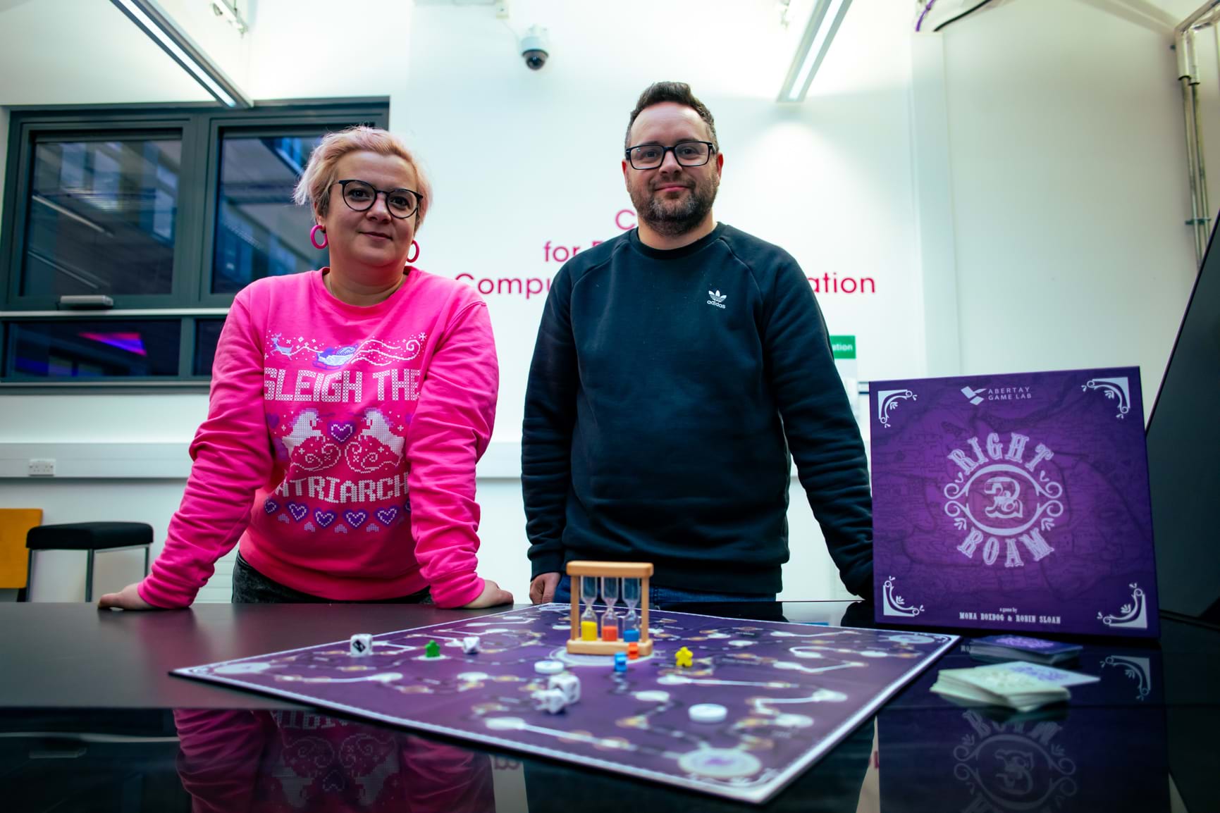 Dr Mona Bozdog wearing a pink jumper and Prof Robin Sloan wearing a blue jumper standing beside the board game