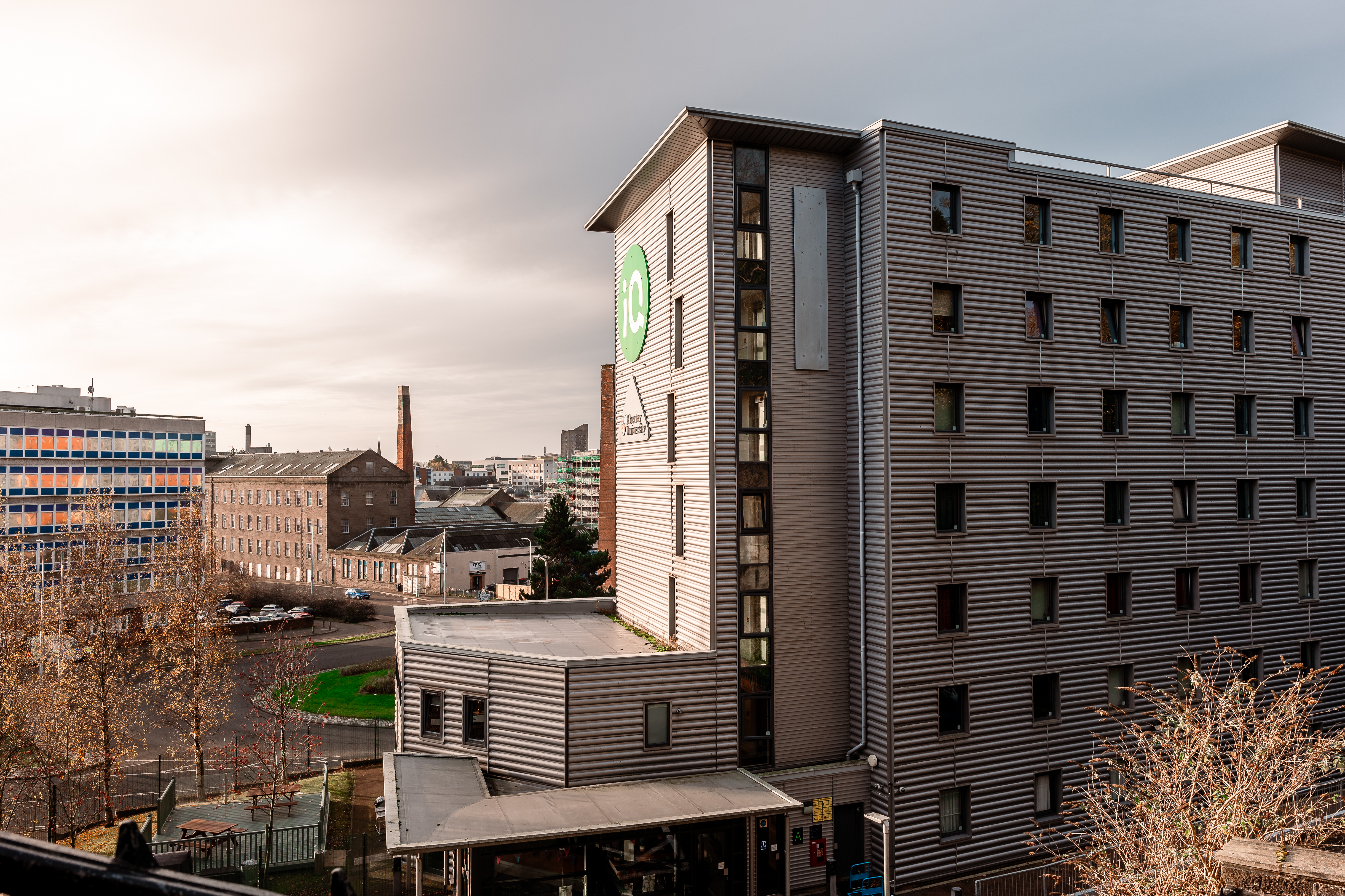 The outside of Parker House student accommodation, a modern grey building, behind you can see other buildings and a road.