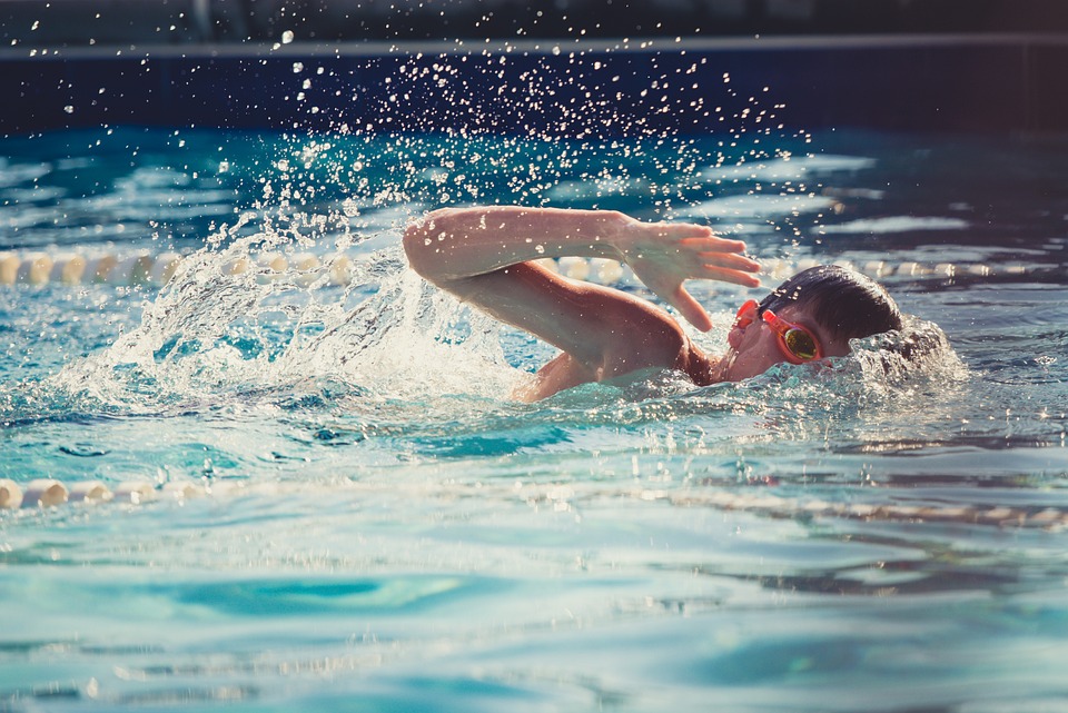 A child swimming in an indoor pool, wearing red goggles